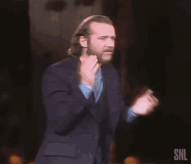 a man in a suit is clapping his hands in front of a snl sign