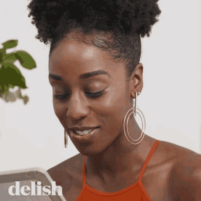 a woman wearing hoop earrings is smiling and looking at a tablet with the word delish below her