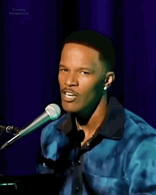 a man in a blue shirt is singing into a microphone in front of a blue curtain that says cinema perspective