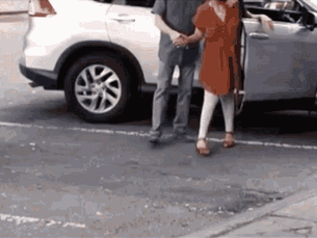 a man and woman are shaking hands in front of a white suv