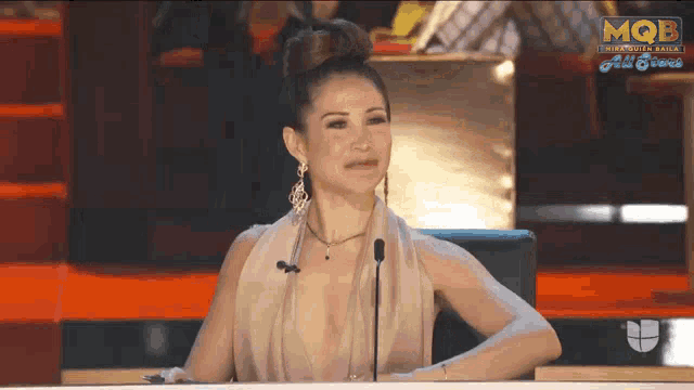 a woman sitting at a table with a microphone in front of a screen that says mqb