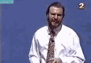 a man with a beard wearing a white shirt and tie is standing in front of a blue background .