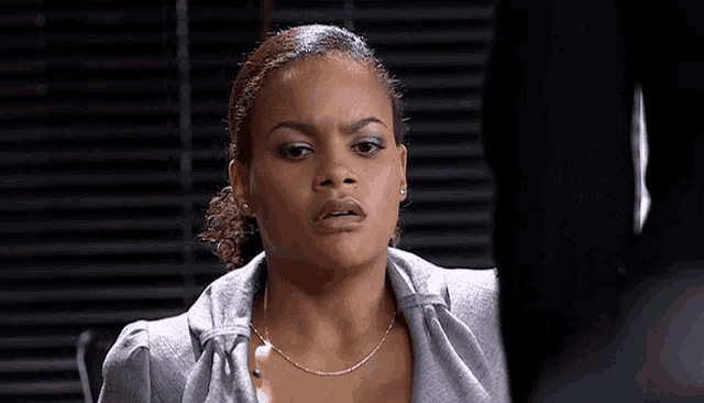 a woman wearing a gray shirt and a silver chain necklace looks at the camera
