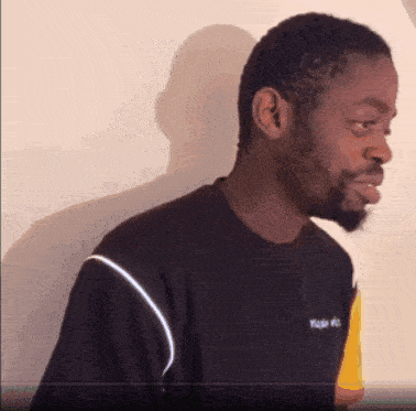 a man with a beard is wearing a black t-shirt with a yellow and white stripe on the sleeve