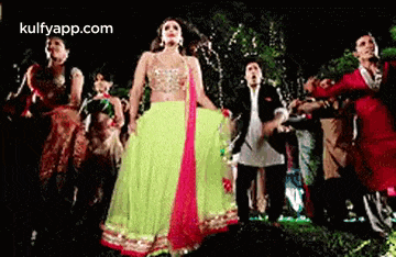 a woman in a green and pink dress is dancing with a group of people in a dark room .