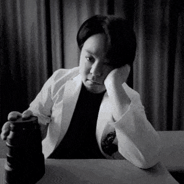a black and white photo of a person sitting at a table holding a camera lens