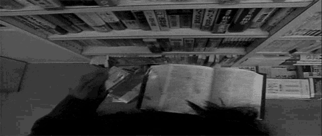 a black and white photo of a person reading a book in front of a shelf of books