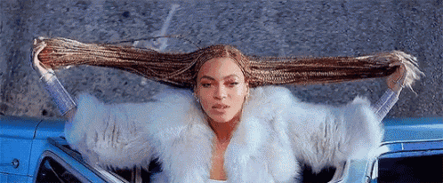 a woman in a fur coat is sitting in a car holding her braids .