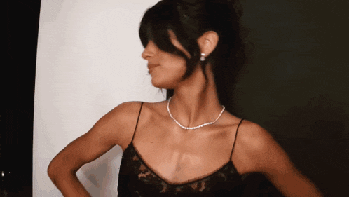 a woman wearing a pearl necklace and earrings stands with her hands on her hips