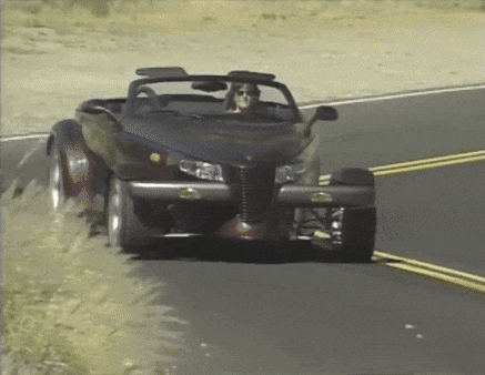 a woman is driving a black convertible car down a road