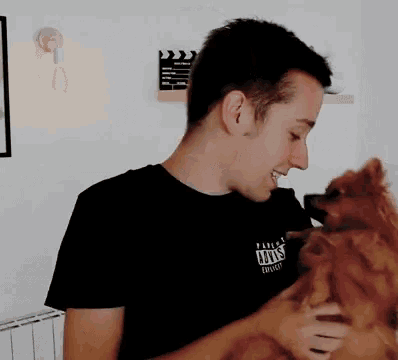 a man in a black shirt with the word vans on it holds a small brown dog