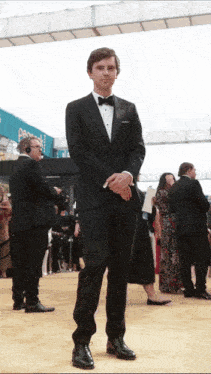 a man in a tuxedo stands on a red carpet