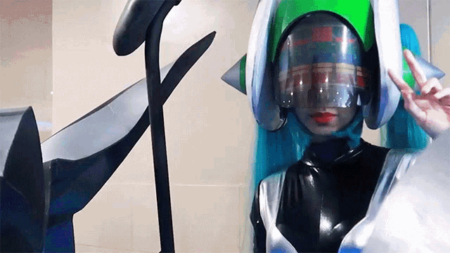 a woman in a futuristic costume with a green helmet giving a peace sign
