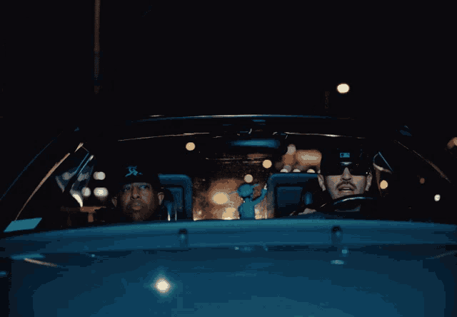 two men are sitting in a car with one wearing a hat that says x on it