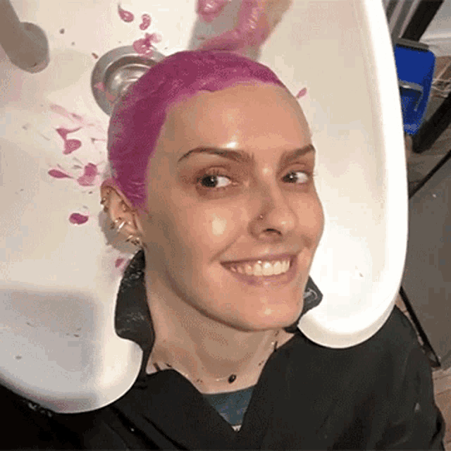 a woman with pink hair is sitting in a sink smiling