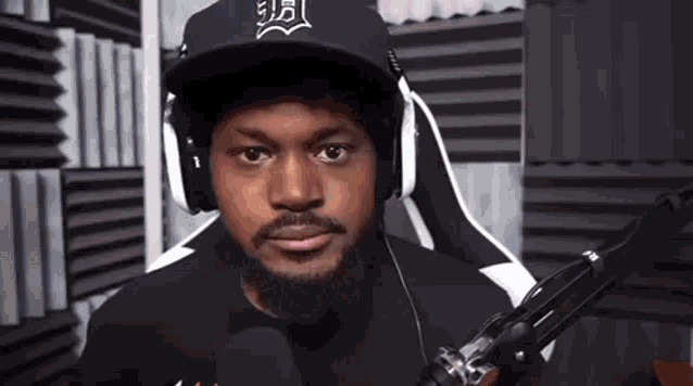 a man with a beard wearing headphones and a hat is sitting in front of a microphone in a room .
