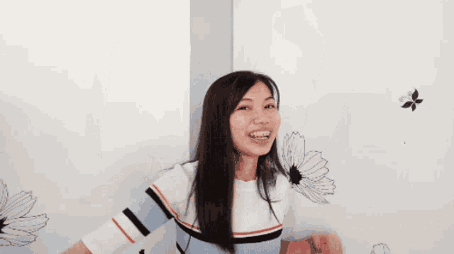 a woman in a striped shirt is standing in front of a white wall with a drawing of a flower on it .