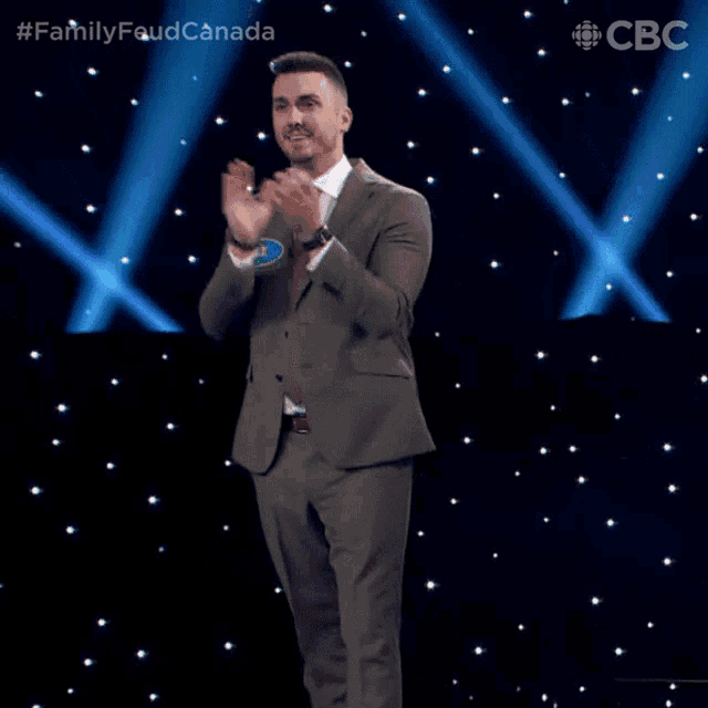 a man in a suit and tie applauds on a stage with a cbs logo in the corner