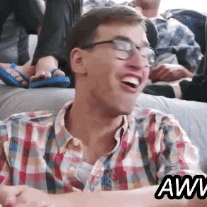 a man wearing glasses and a plaid shirt is sitting on a couch and smiling