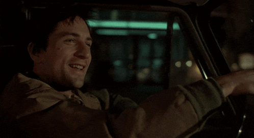 a man in a tan jacket is smiling while driving a car at night