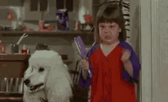 a little girl is brushing her hair next to a white poodle