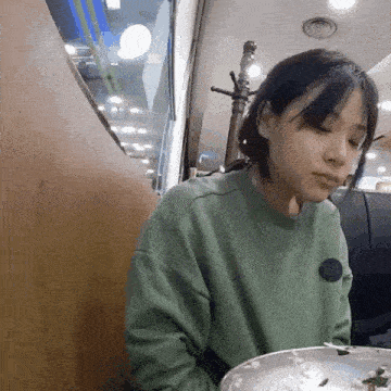 a woman in a green sweater is sitting at a table with a bowl of food .