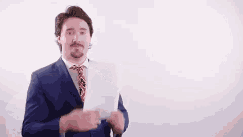 a man in a suit and tie is holding a piece of paper in front of his face .