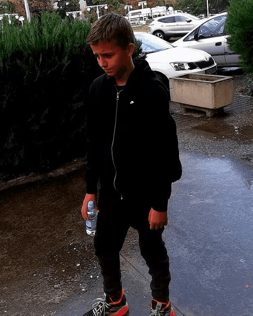a young boy in a black nike jacket holds a water bottle