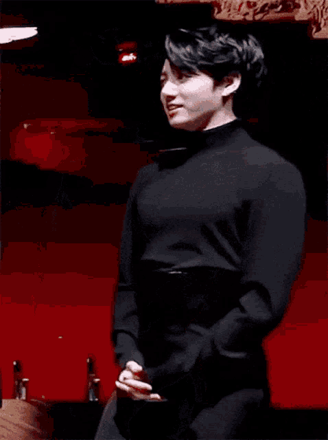 a man in a black turtleneck sweater is standing in front of a red wall