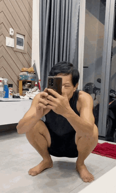 a man squatting down taking a selfie with his phone