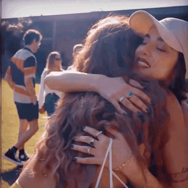 a woman wearing a hat is hugging another woman in a field