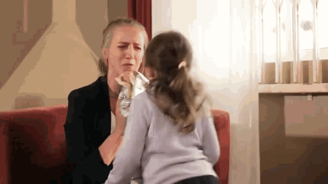 a woman is sitting on a couch talking to a little girl who is crying .