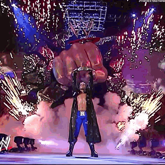 a wrestler with the letter r on his belt is standing in front of a giant hand .