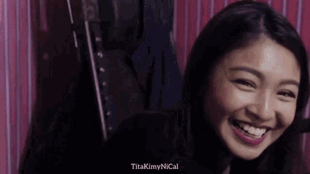 a woman is smiling in front of a pink wall and the words titakynnyical are visible