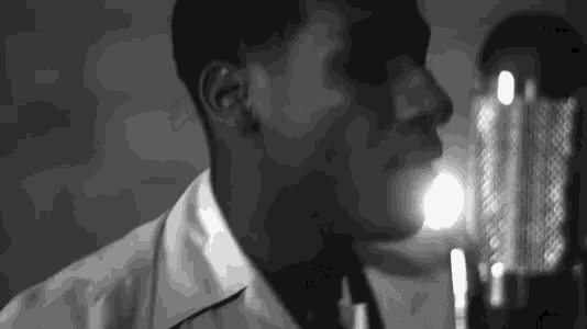 a man in a white shirt and tie is singing into a microphone .