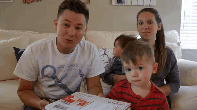 a family sitting on a couch with a man wearing a shirt that says am world