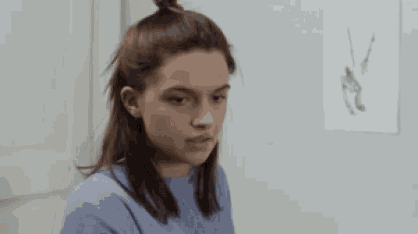 a young woman in a blue sweater is sitting in front of a wall with a drawing on it .