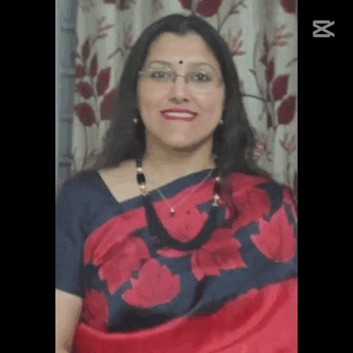 a woman in a red and black floral saree and glasses is smiling .