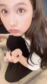 a woman with long black nails is sitting on a couch looking at the camera