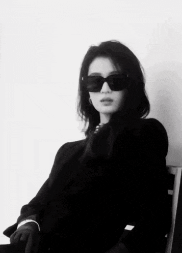 a woman wearing sunglasses and a black sweater is sitting in a chair