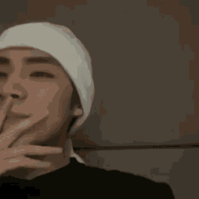 a young man wearing a white beanie and a black shirt is smoking a cigarette .