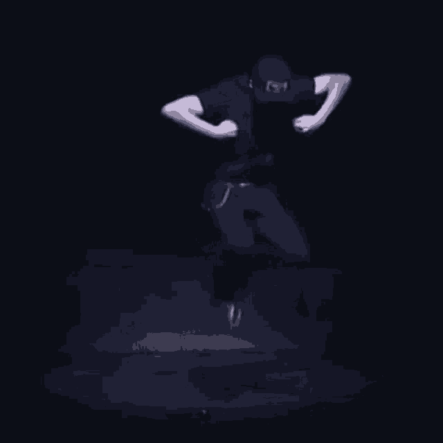 a man wearing a hat and a black shirt is dancing on a stage in the dark .