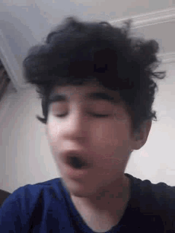 a young boy with curly hair is yawning with his mouth open .