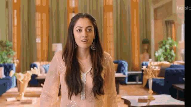 a woman in a white dress is standing in a living room with a lot of furniture .