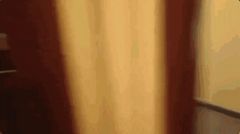 a person is standing in front of a window in a room with a yellow curtain .