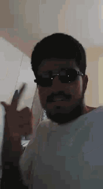 a man with a beard is wearing sunglasses and giving a peace sign .