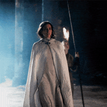 a woman in a white cape stands in the dark