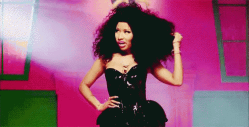 a woman with curly hair is standing in a pink room wearing a black dress .