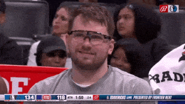 a man wearing glasses sits in the stands watching a basketball game