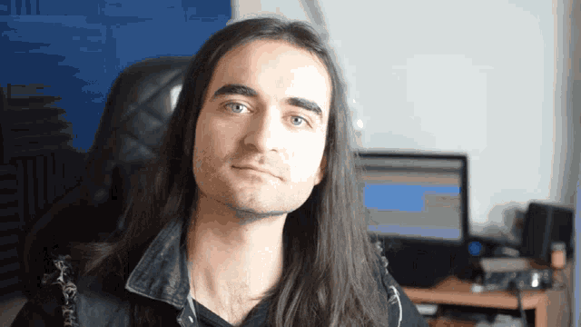 a man with long hair is sitting in a chair in front of a computer